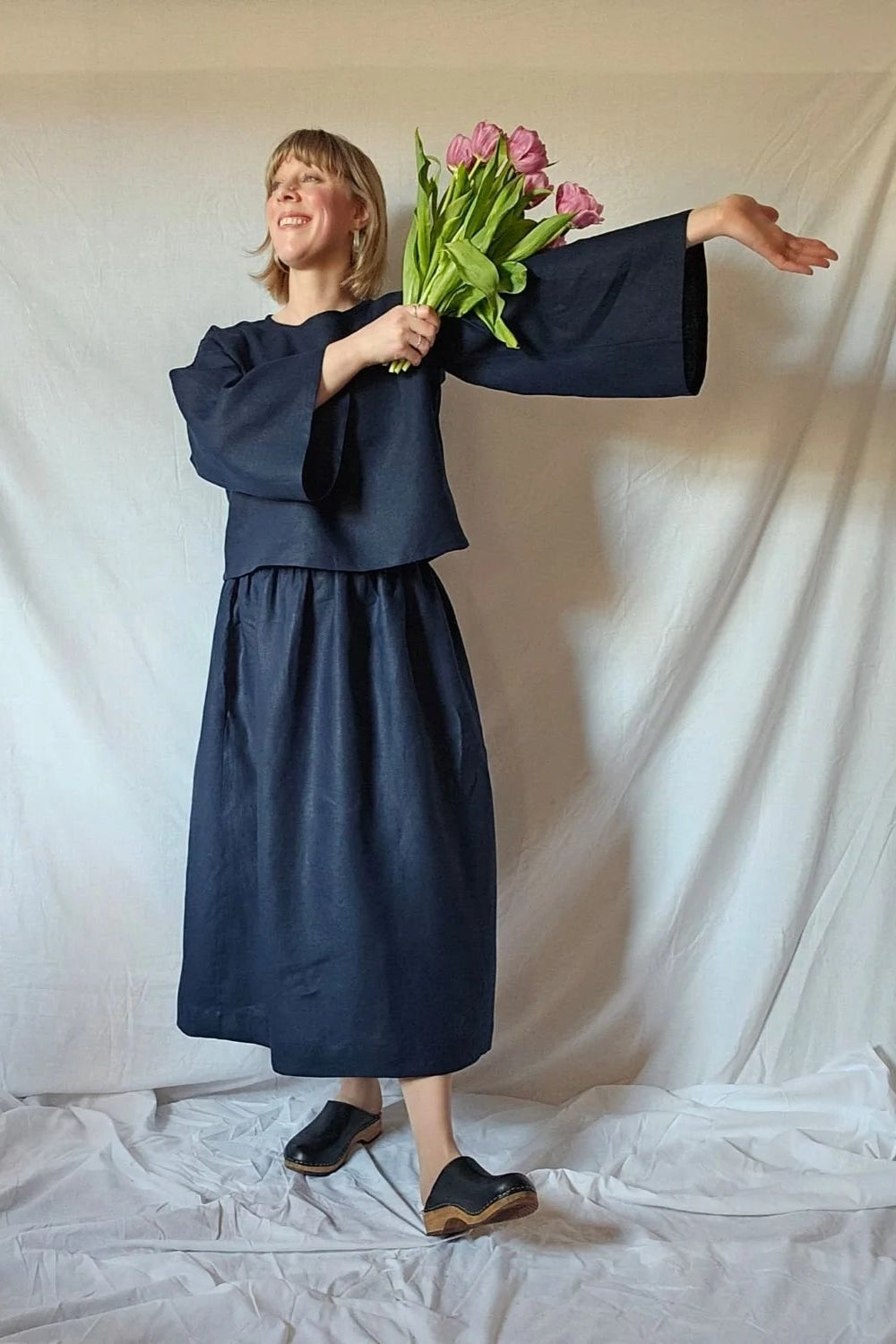 Person wearing a navy blue outfit holding pink tulips against a white backdrop