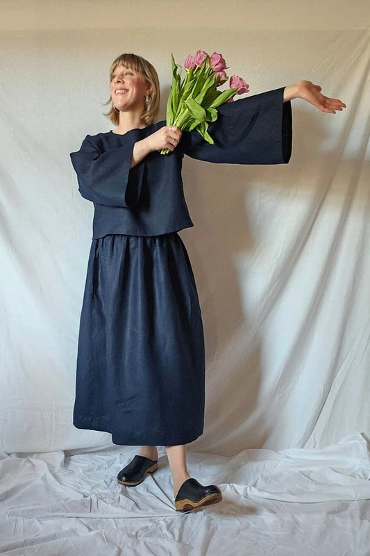 Person wearing a navy blue outfit holding pink tulips against a white backdrop