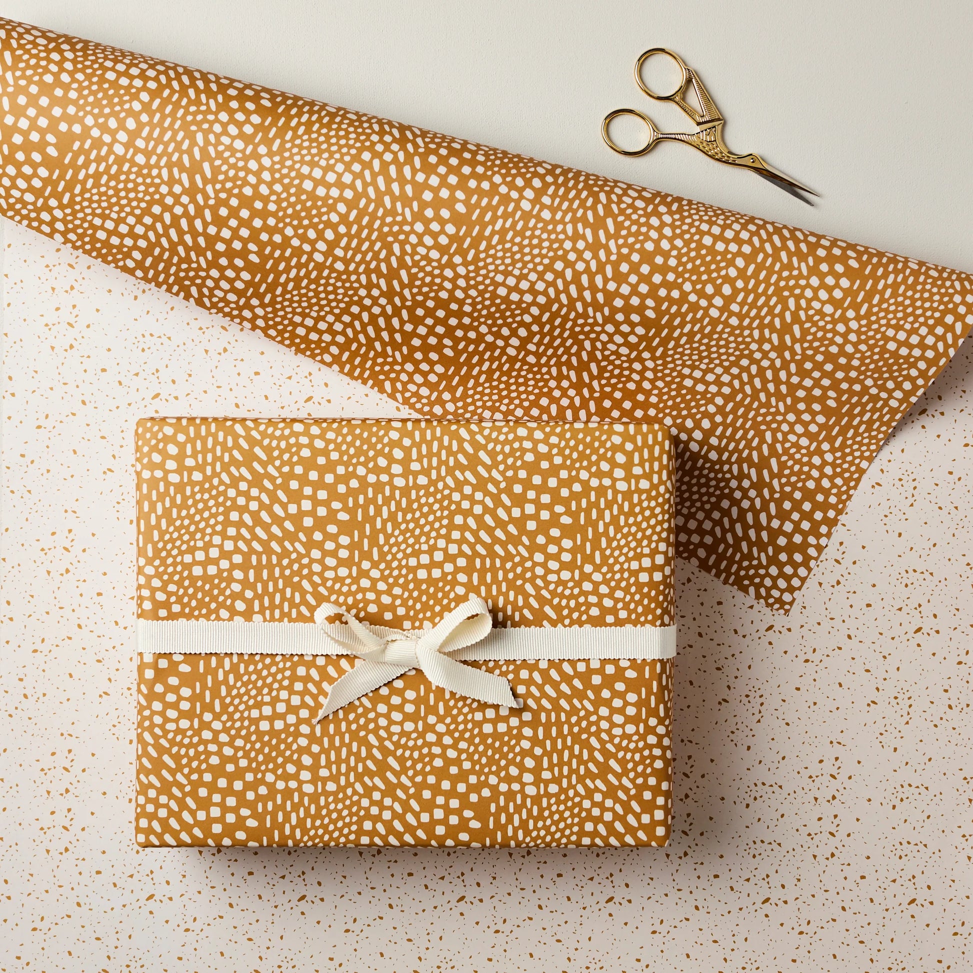 Gift wrapped in brown paper with white pattern and tied with a ribbon, on a light background.