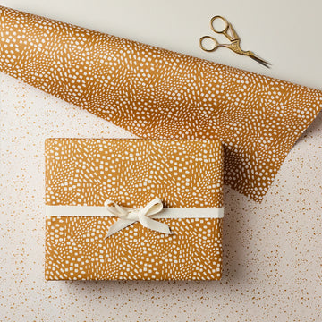 Gift wrapped in brown paper with white pattern and tied with a ribbon, on a light background.