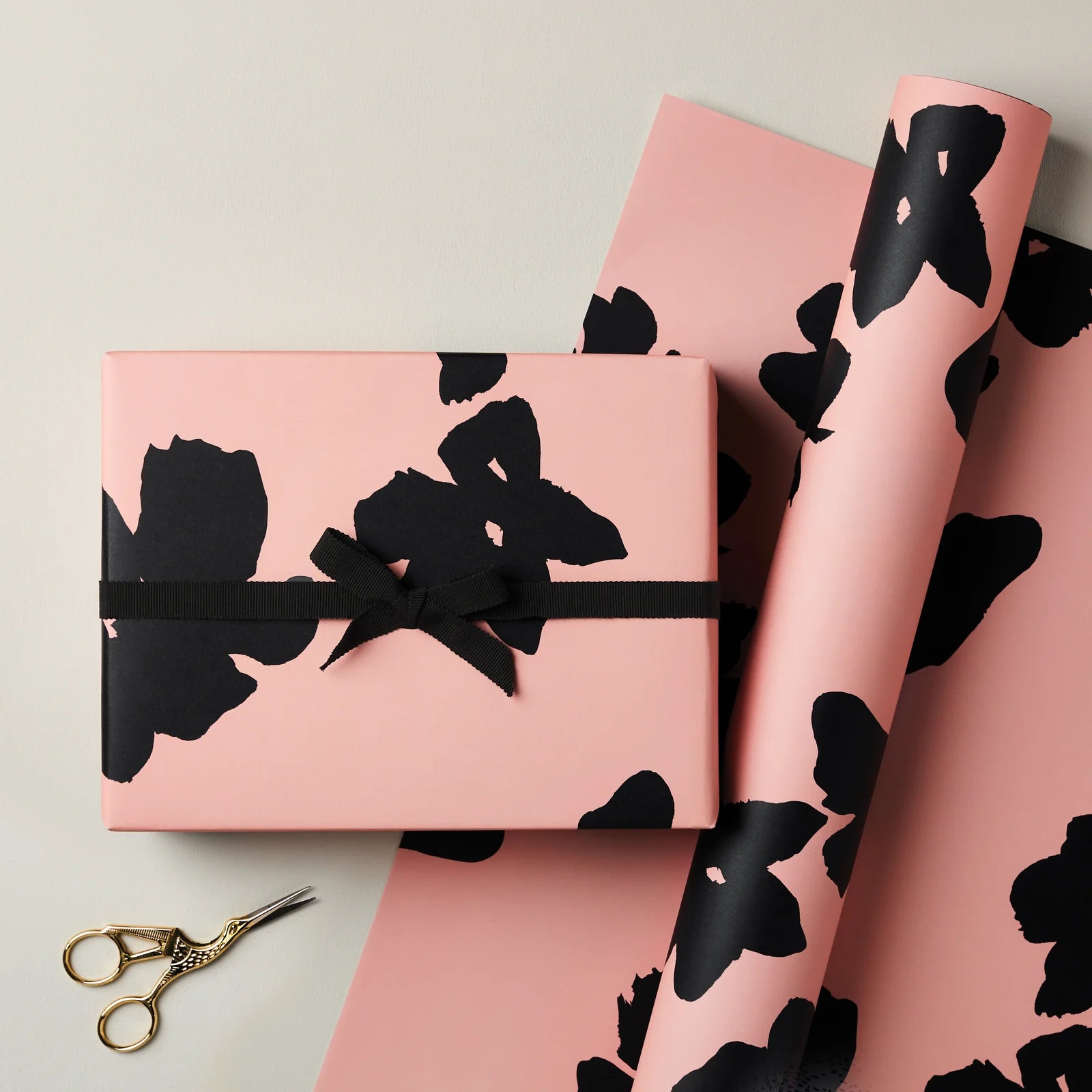 Pink gift box and wrapping paper with black floral patterns on a light gray background