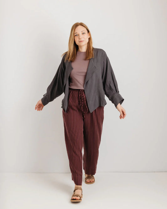 Woman wearing a grey jacket, brown t-shirt, and striped trousers on a white background