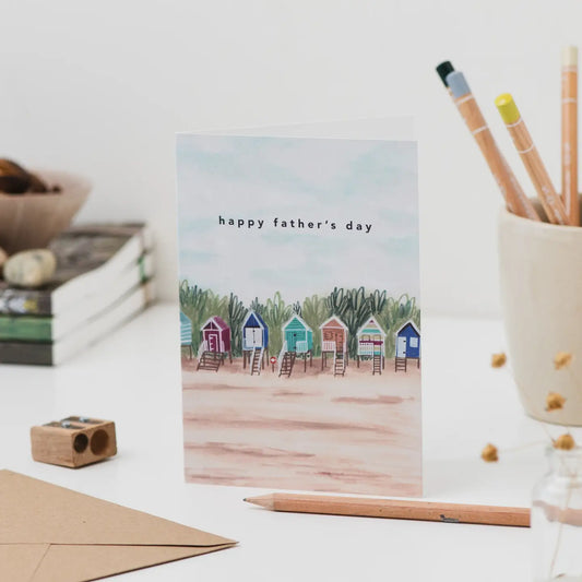 Father's Day card with beach huts design on a desk with stationery items.
