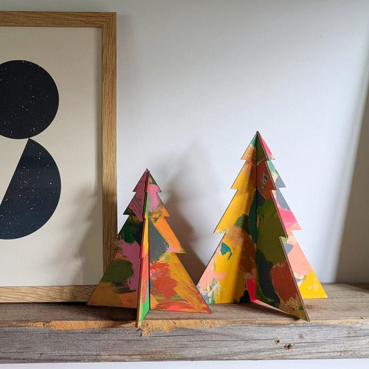 Colorful triangular wooden sculptures on a wooden surface with a framed abstract art piece in the background.