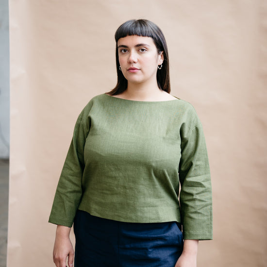 Woman wearing a green top and blue pants against a beige background