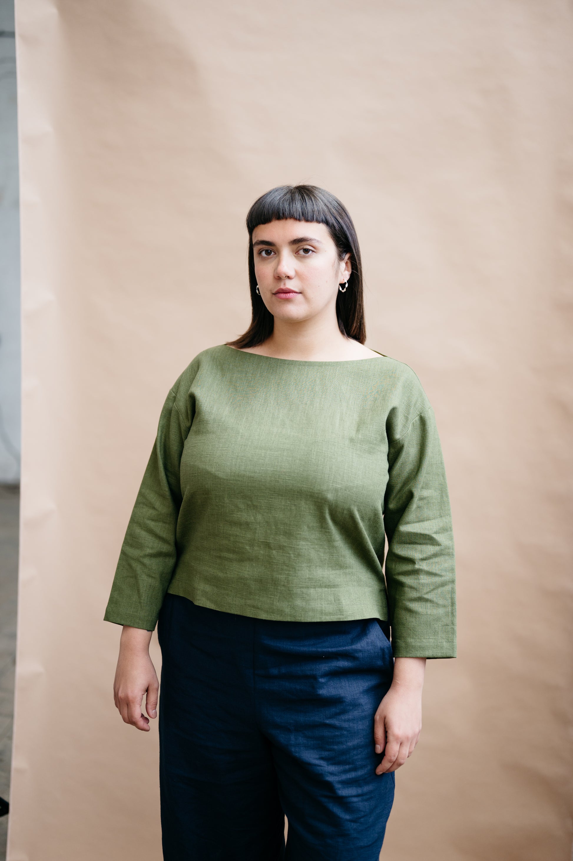 Woman wearing a green top and blue pants against a beige background