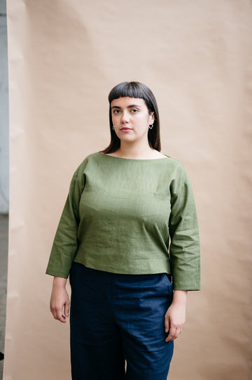 Woman wearing a green top and blue pants against a beige background