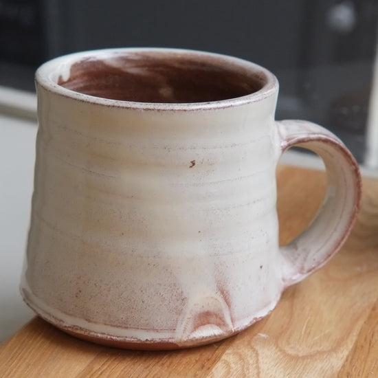 A handmade ceramic mug with a textured, ribbed surface and a rustic finish, sitting on a wooden tabletop.