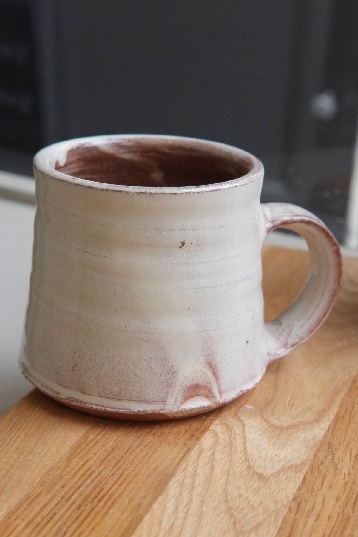 A handmade ceramic mug with a textured, ribbed surface and a rustic finish, sitting on a wooden tabletop.