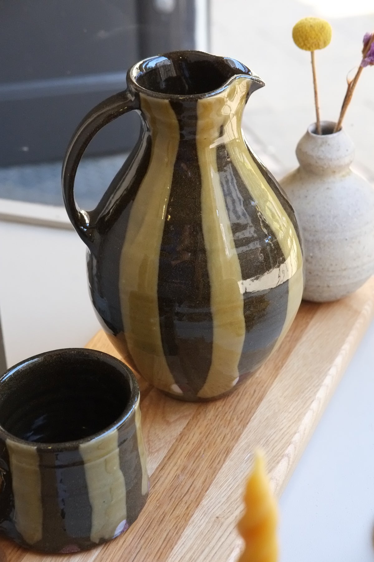 Green stripe ceramic jug with a rounded body and spout on a wooden board surrounded by other ceramics