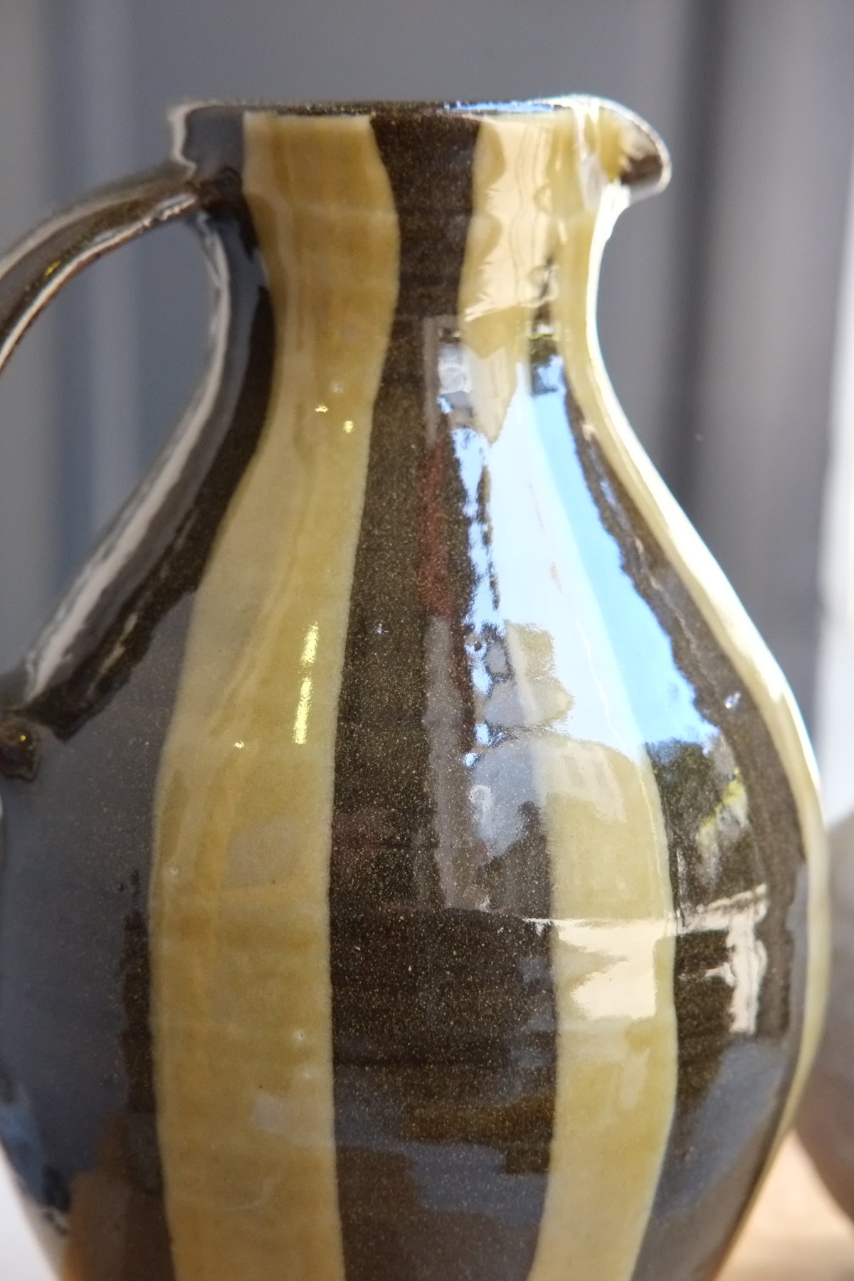 A close-up of a handmade ceramic pitcher with a glossy finish, featuring vertical stripes of dark brown and green