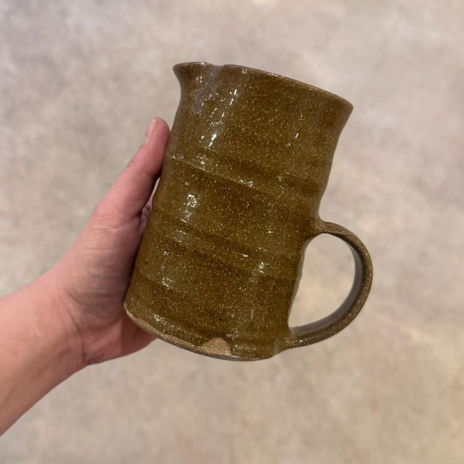 Hand holding a brown ceramic mug against a neutral background