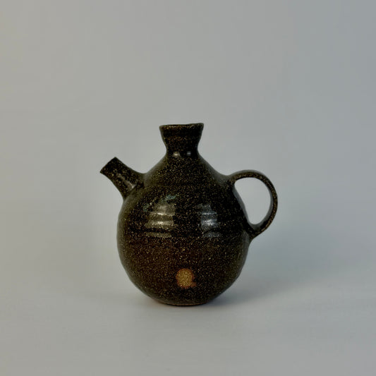 Brown ceramic oil pourer with a handle on a gray background