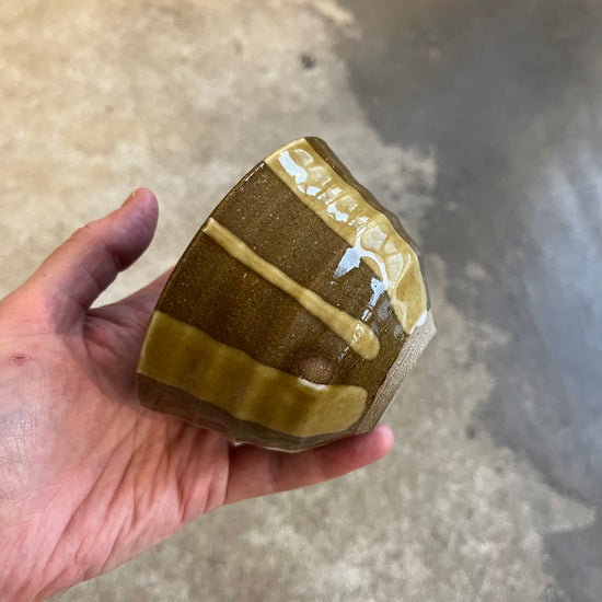 A hand holding a small red and green striped ceramic pot with a nico glaze finish.