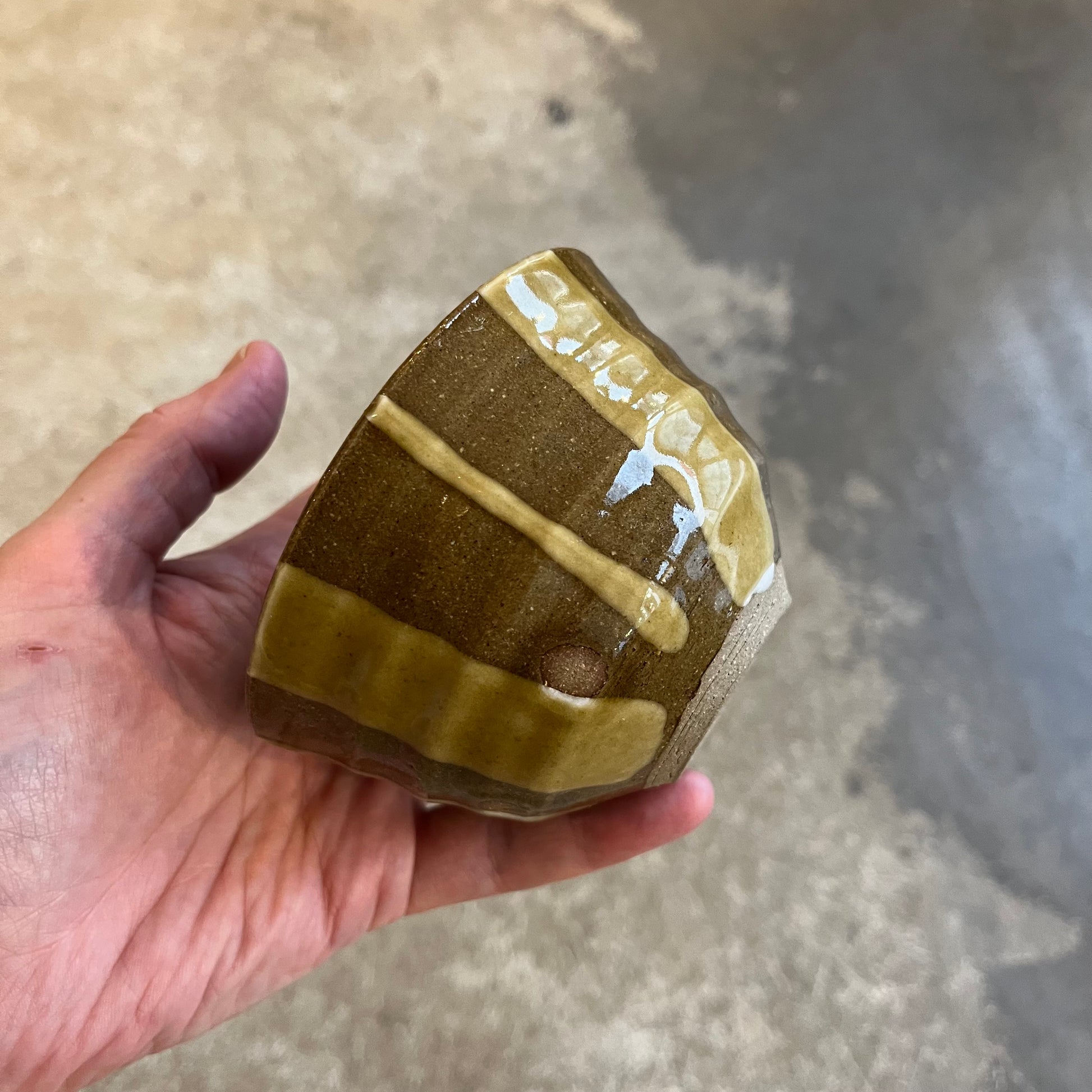 A hand holding a small red and green striped ceramic pot with a nico glaze finish.