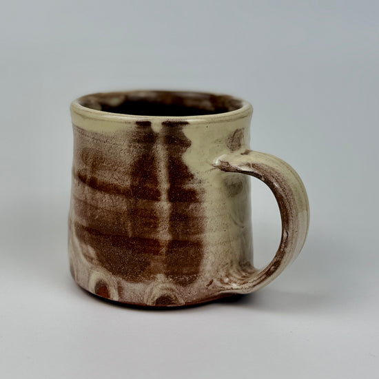 Ceramic mug with brown and beige glaze on a gray background