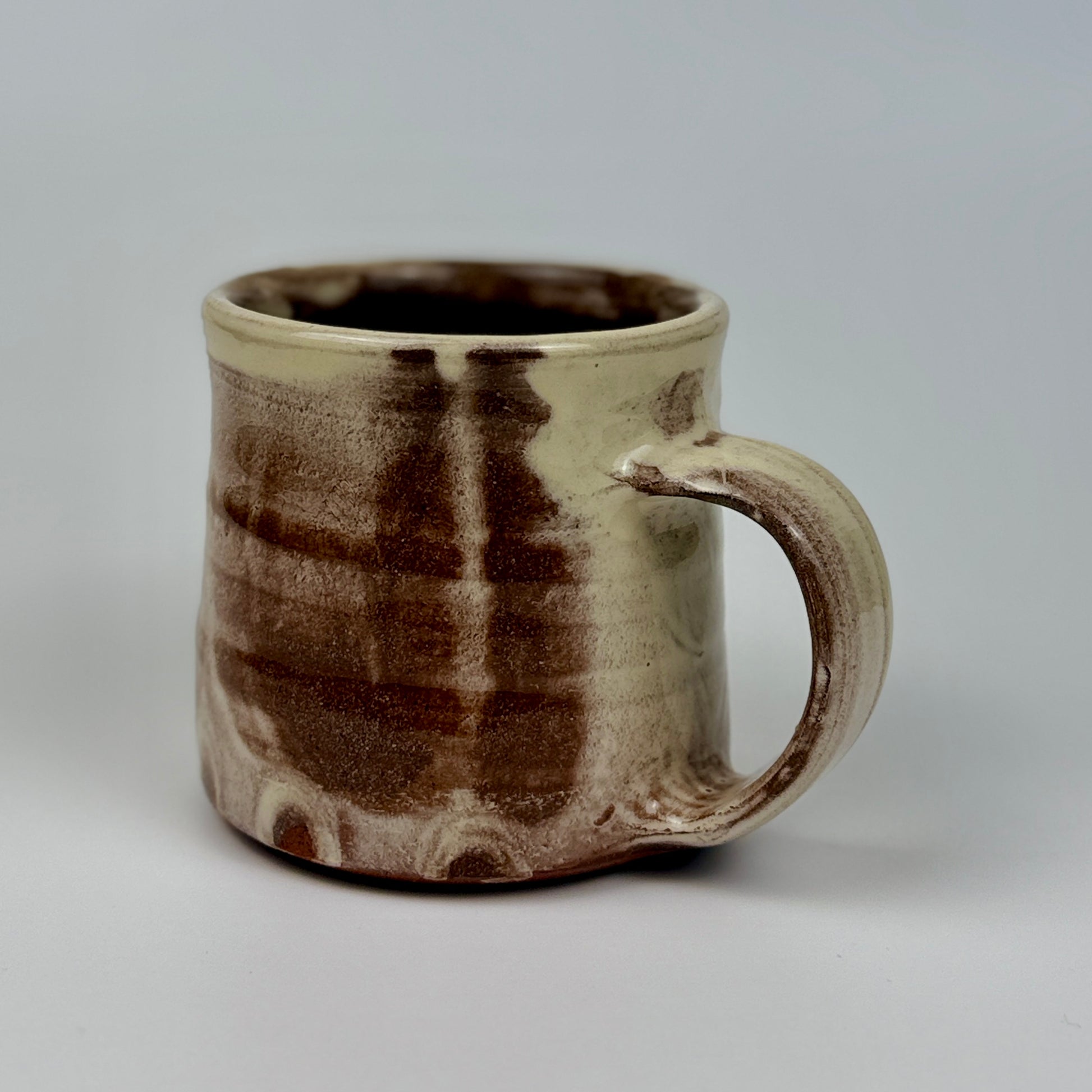 Ceramic mug with brown and beige glaze on a gray background