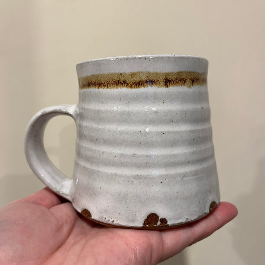 Hand holding a grey ceramic mug with a brown accent against a plain background