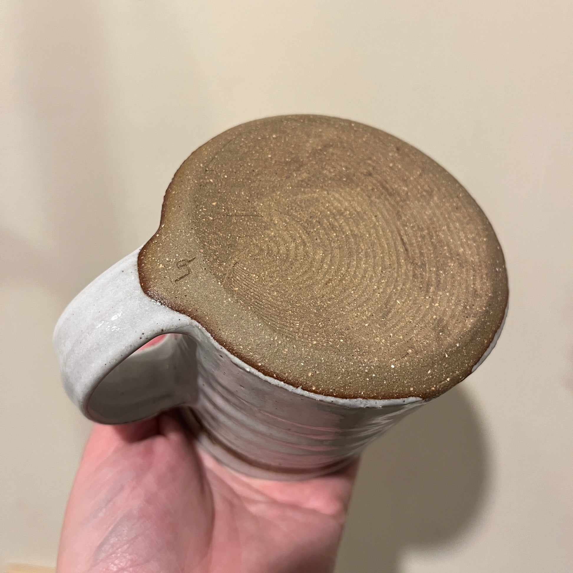 Ceramic grey mug with texture base held in a hand against a neutral background