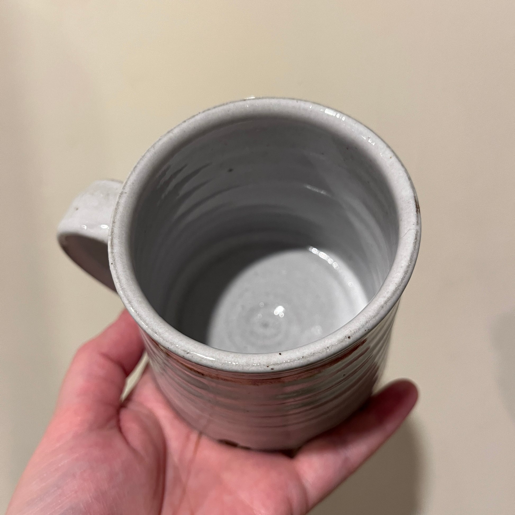 Hand holding a grey ceramic mug against a beige background