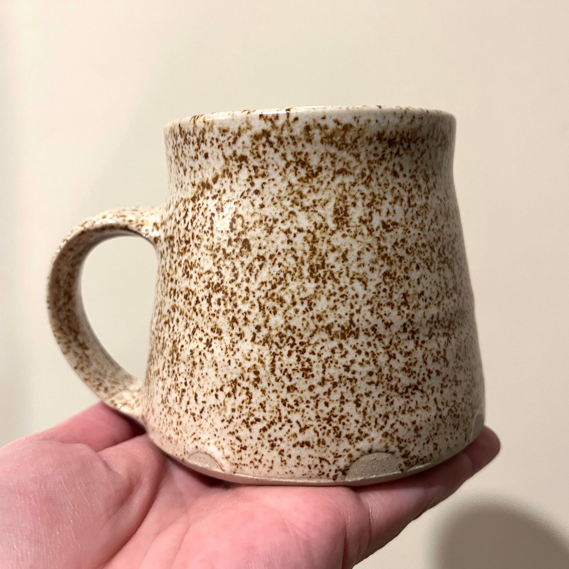 Speckled ceramic mug held in a hand against a plain background