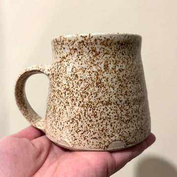 Speckled ceramic mug held in a hand against a plain background