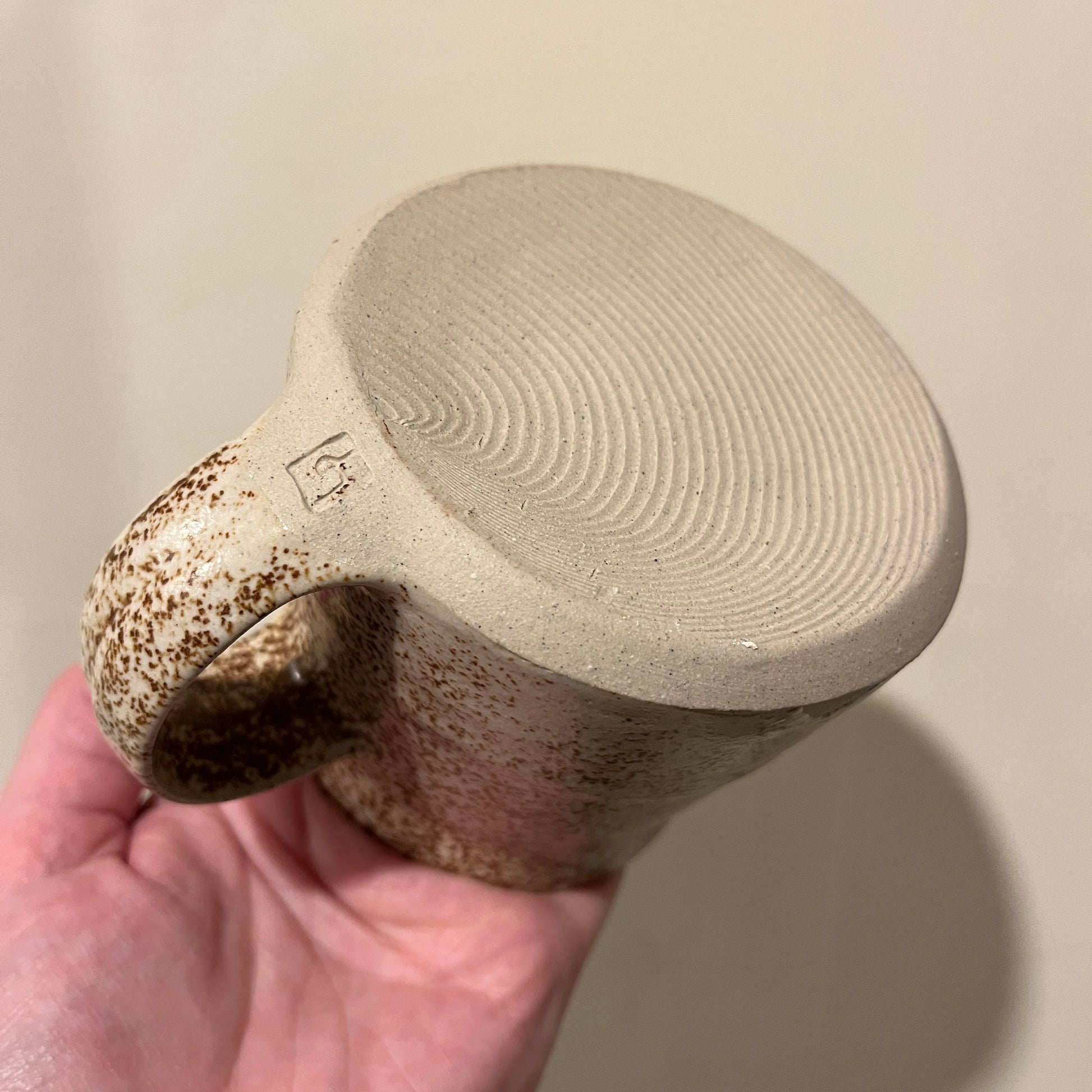 Ceramic mug with textured surface base and speckled handle held by a hand against a neutral background