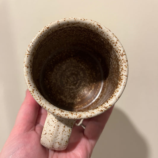 Hand holding a ceramic mug with brown speckles against a plain background