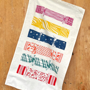 A tea towel with multicolour crackers on the front on a brown backgorund 