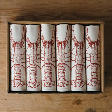 Set of six napkins with red lobster illustrations on a wooden surface
