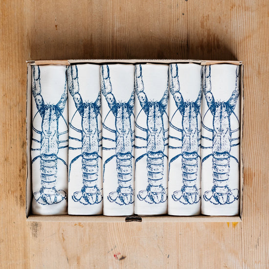 Set of white napkins with blue lobster design in a wooden box on a wooden surface