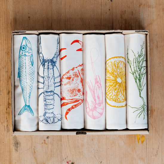 Set of five napkins with food illustrations in a box on a wooden surface