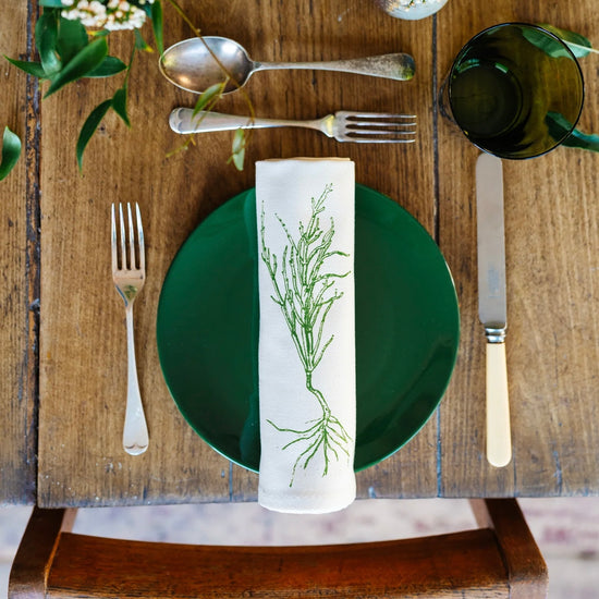 Table setting with green plate, silverware, and a decorative napkin on a wooden table.
