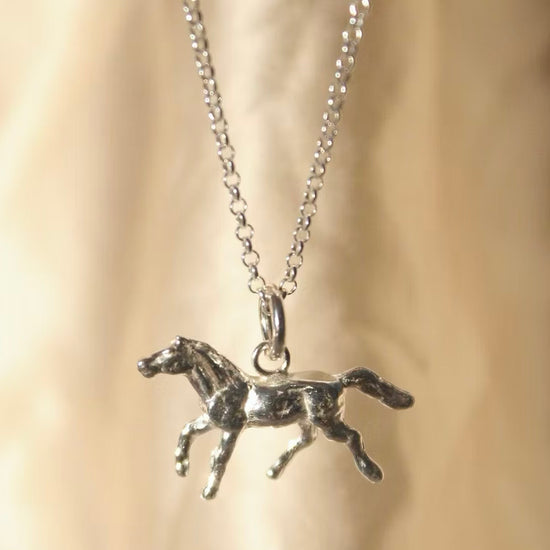 solid silver pony charm on a silver chain hanging in front of a cream background