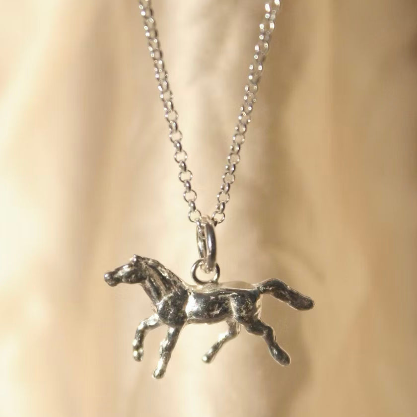 solid silver pony charm on a silver chain hanging in front of a cream background