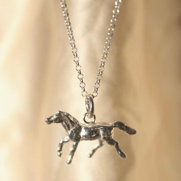 solid silver pony charm on a silver chain hanging in front of a cream background