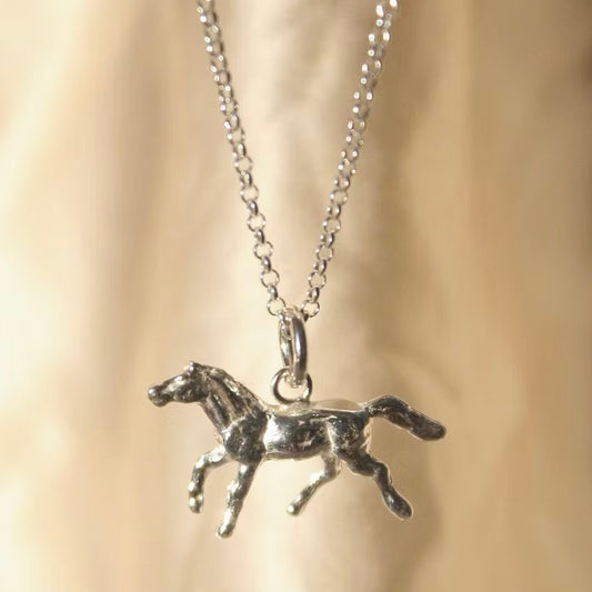 solid silver pony charm on a silver chain hanging in front of a cream background
