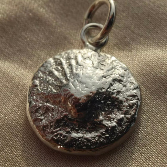 solid silver pendant charm with scallop detail on a woven beige background