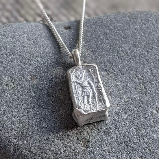 solid silver pendant necklace with an acient coin design debossed on a silver chain, against a stone background