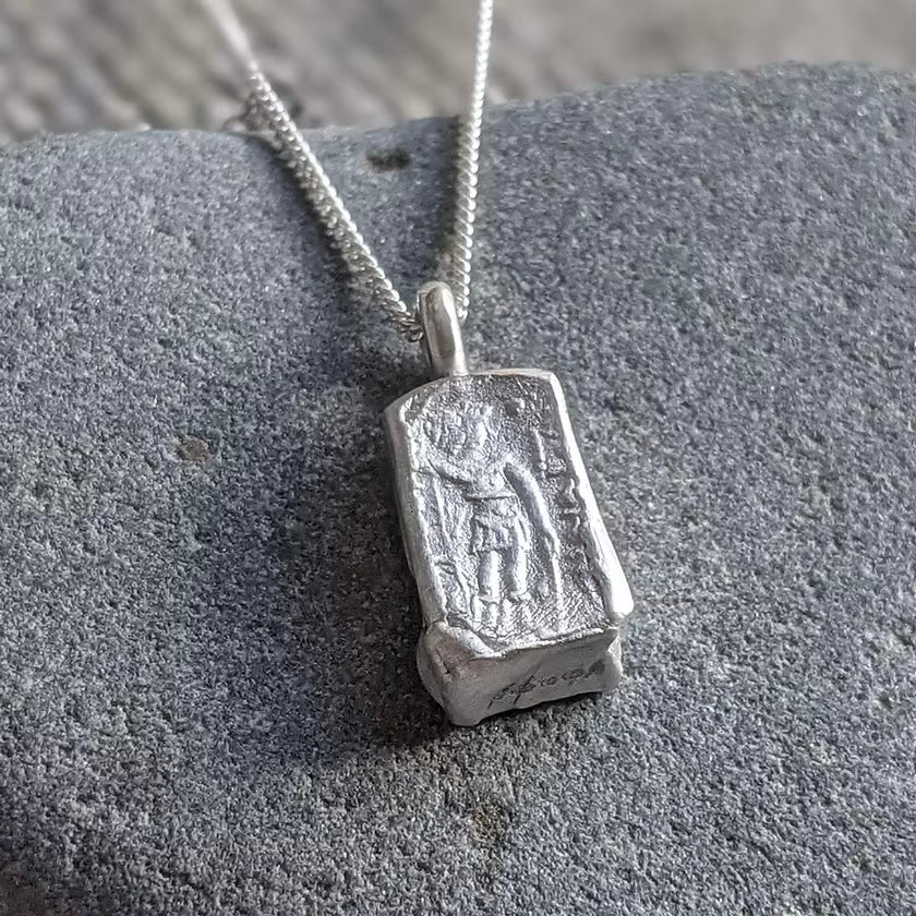 solid silver pendant necklace with an acient coin design debossed on a silver chain, against a stone background