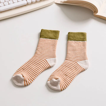Pair of striped beige and mustard and olive socks on a desk with a keyboard and book in the background