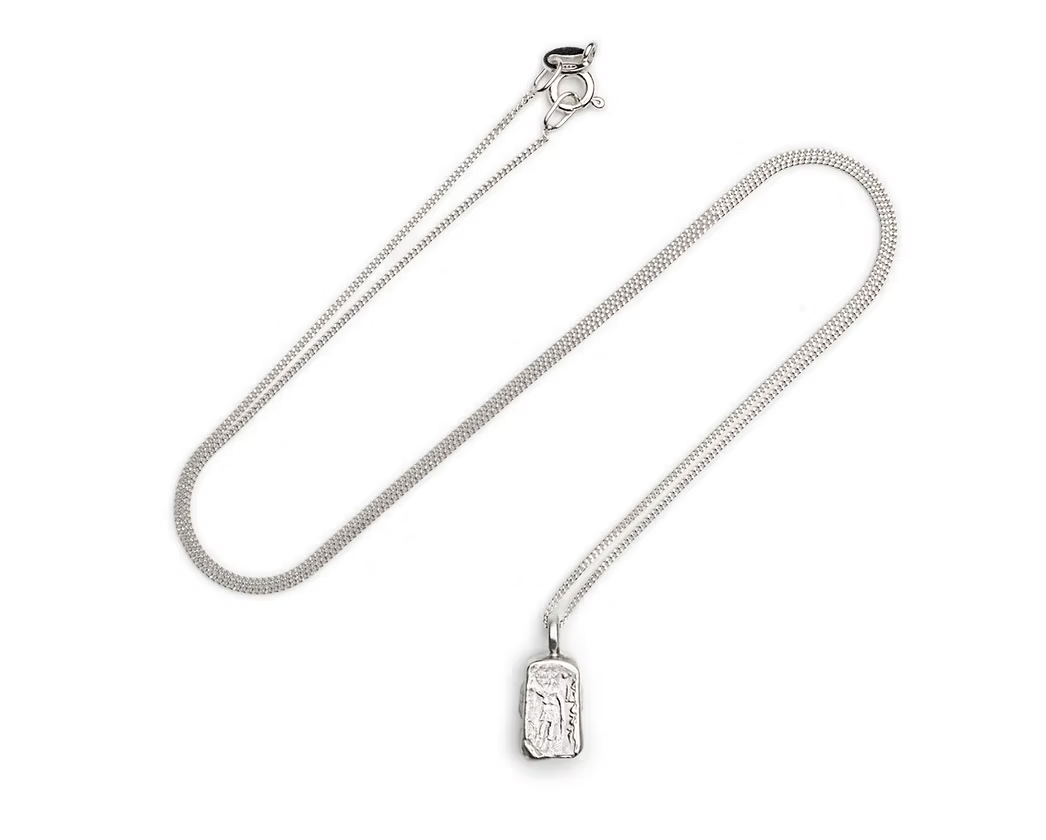 A silver  chain necklace with a small rectangular pendant featuring an embossed figure, displayed on a clean white background.
