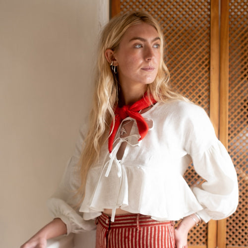 Woman wearing a white blouse with a red scarf and red striped pants, standing indoors.