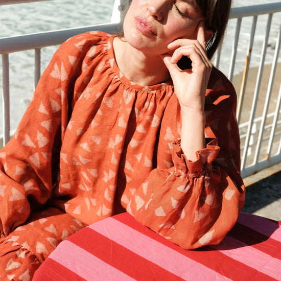 Woman in an orange dress sitting at a table with striped tablecloth by the sea.