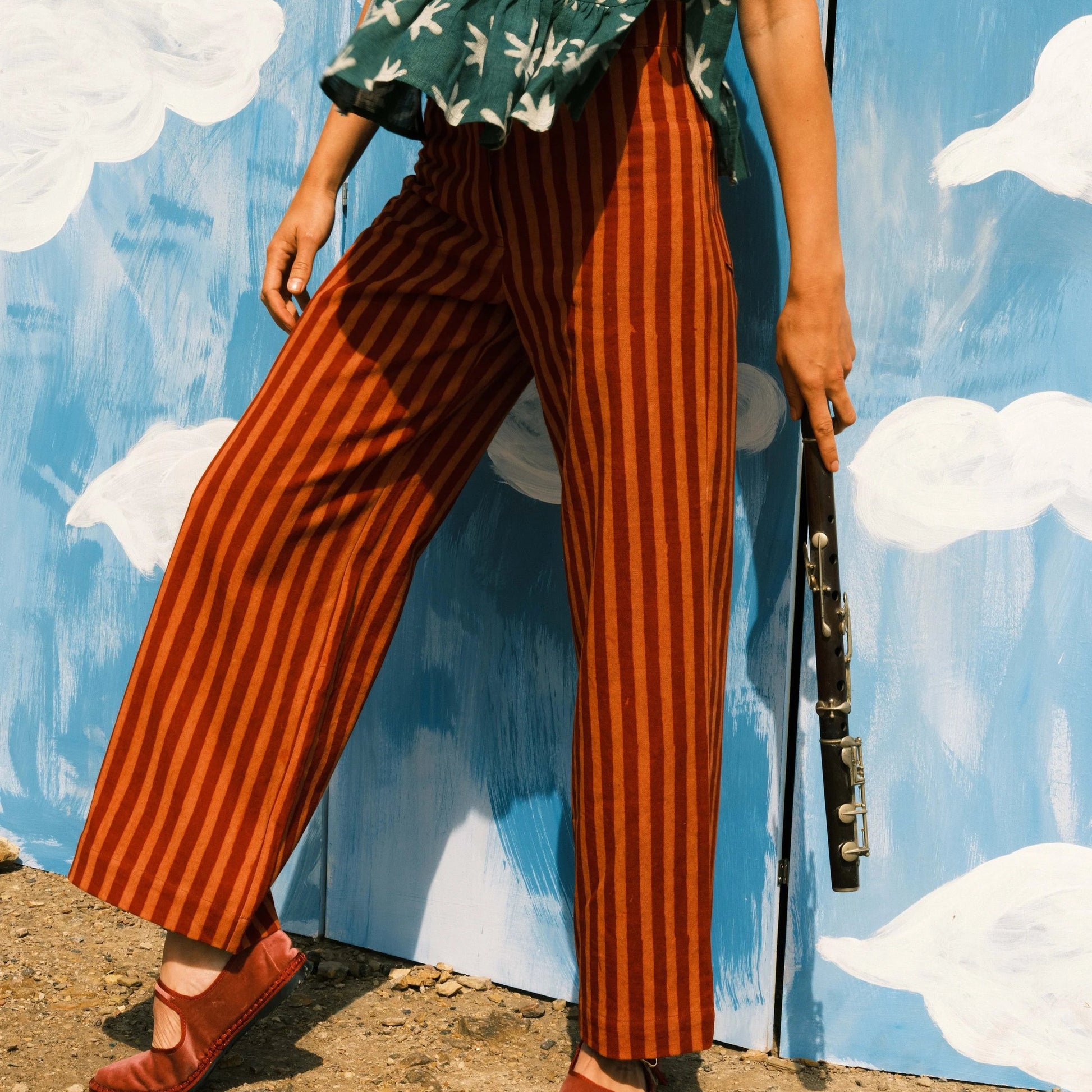 Person wearing a green floral top and red striped pants against a blue wall with white clouds.