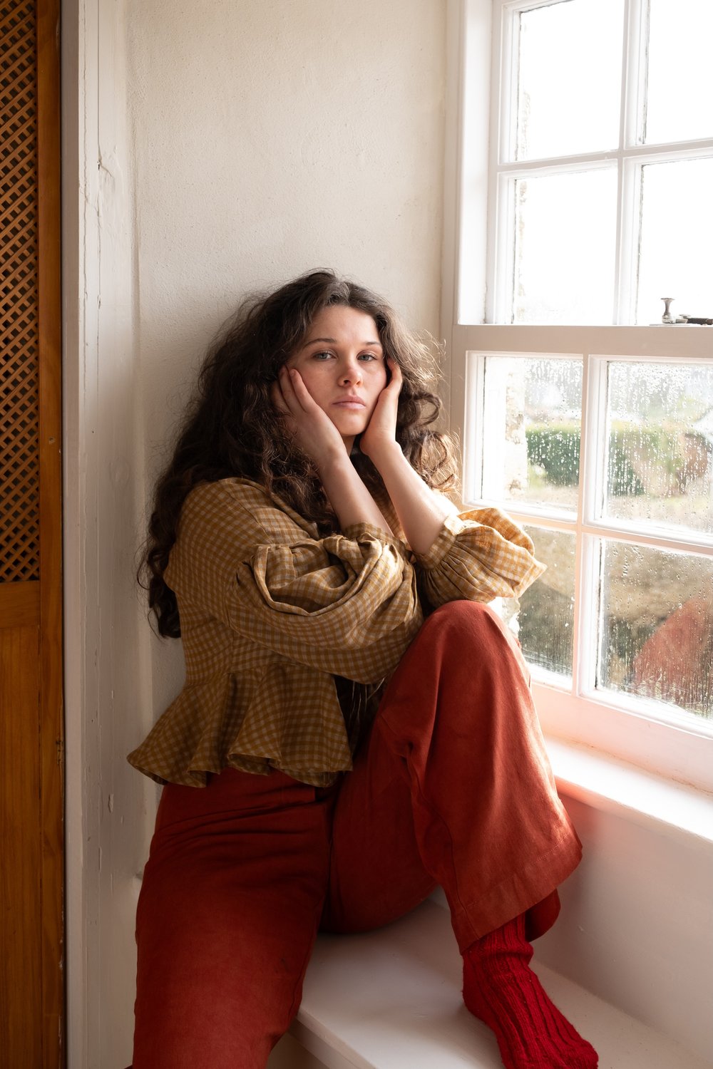 woman wearing flaxen linen top sitting on window sill