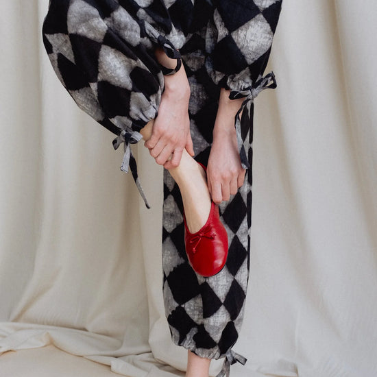 Person wearing black and white checkered pants with red shoes against a neutral background