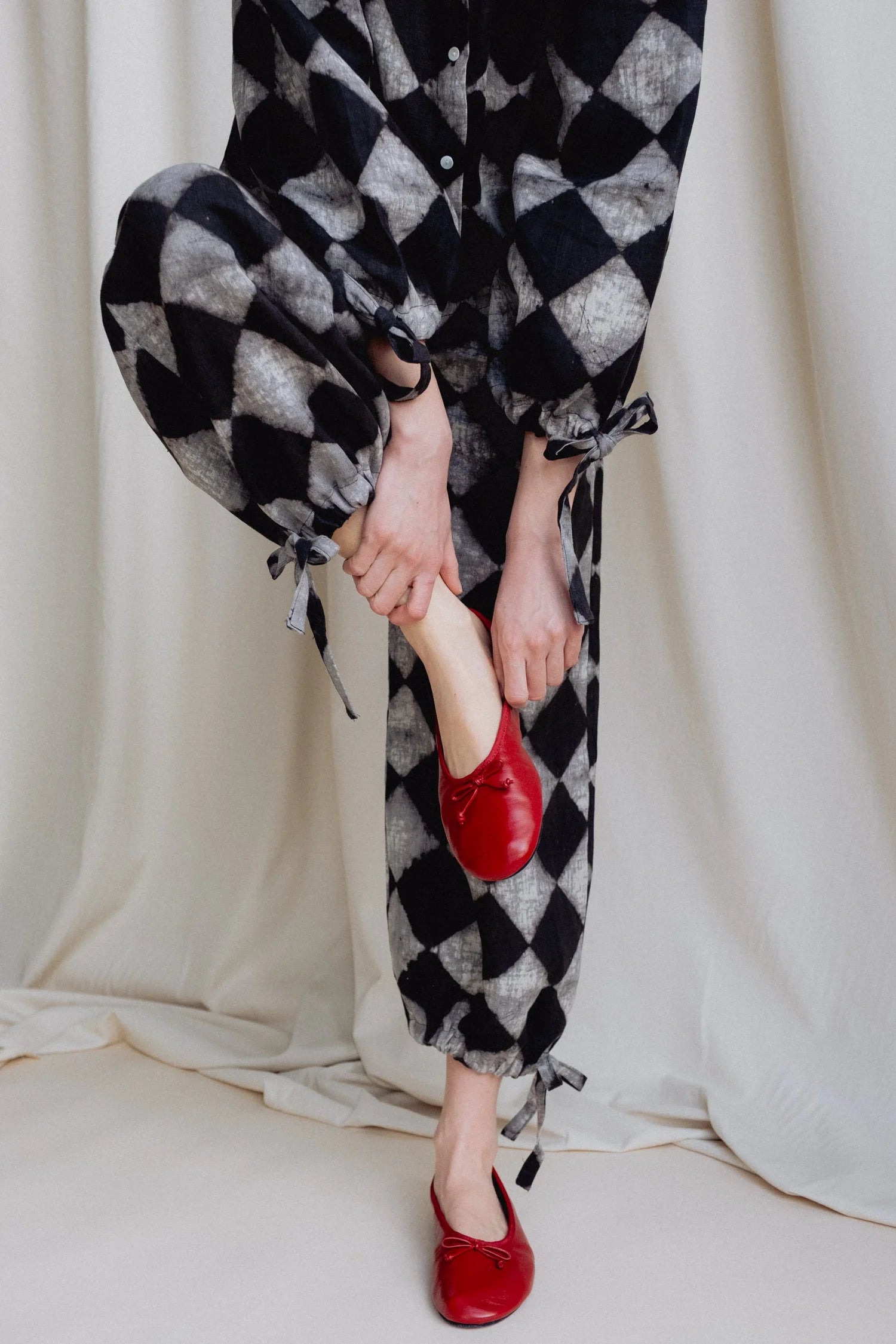 Person wearing black and white checkered pants with red shoes against a neutral background