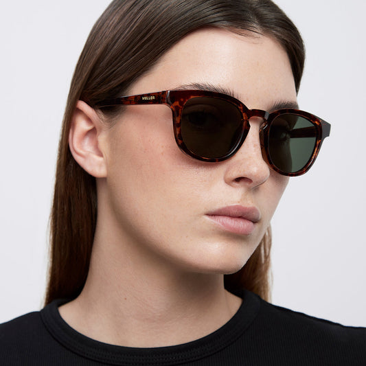 A woman wearing dark sunglasses on a white background 