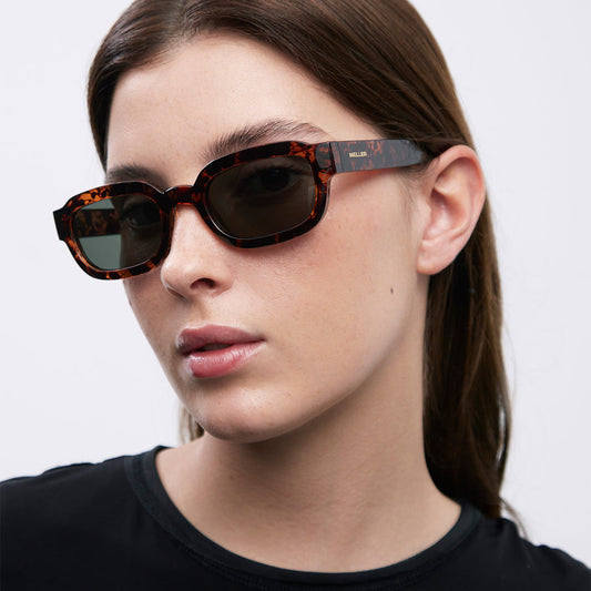 A woman with dark hair wearing sunglasses on a white background 